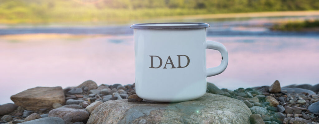 A tin cup saying Dad on a rock besides a lake. 