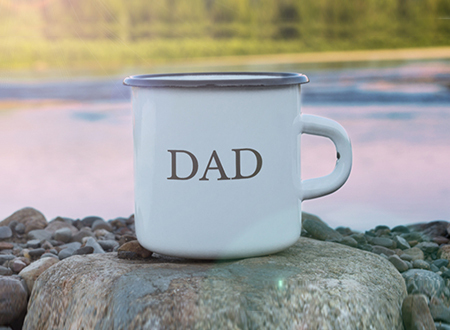 A tin cup saying Dad on a rock besides a lake.
